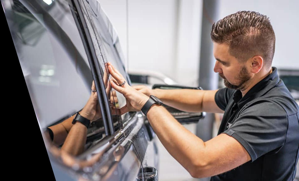 An auto technician installs window tint on the passenger side of a vehicle 