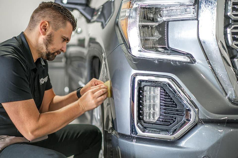 An auto technician applies protective coating to the side of a vehicle